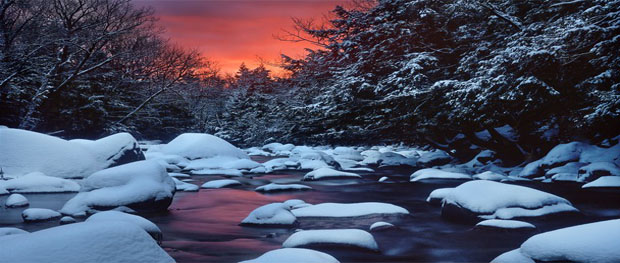 Snowy rocks accent a river in a New Hampshire forest at sunset
